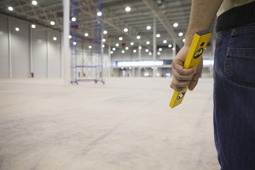Man stands holding spirit level in empty warehouse