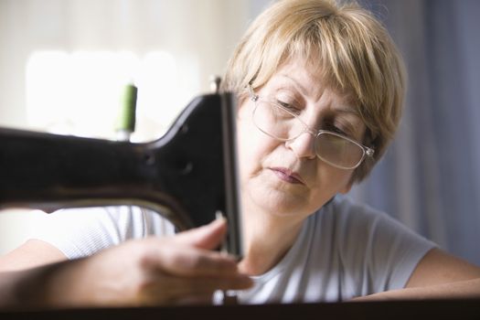 Mature woman adjusts foot of sewing machine