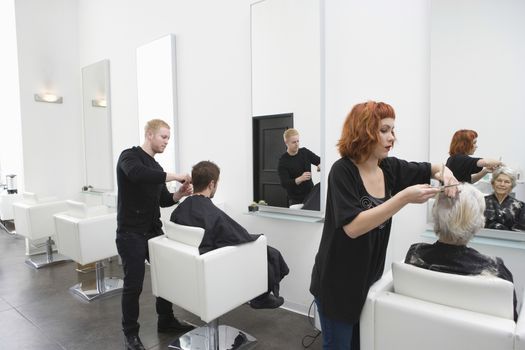 Hairdressers giving haircut to customers in unisex salon