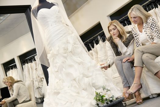 Mother and daughter sitting on sofa while looking at elegant wedding dress in bridal store