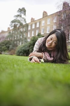 Portrait of a young woman with flower lying lawn in front of building
