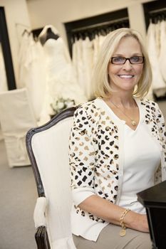 Portrait of a happy senior female wearing eyeglasses sitting in bridal boutique