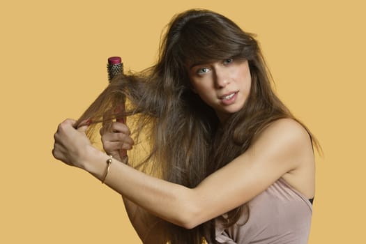 Portrait of a young woman brushing hair over colored background