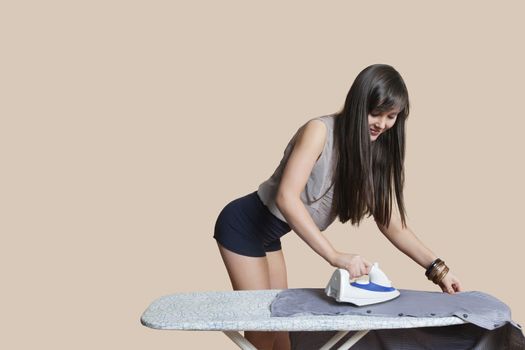 Young woman ironing shirt over colored background
