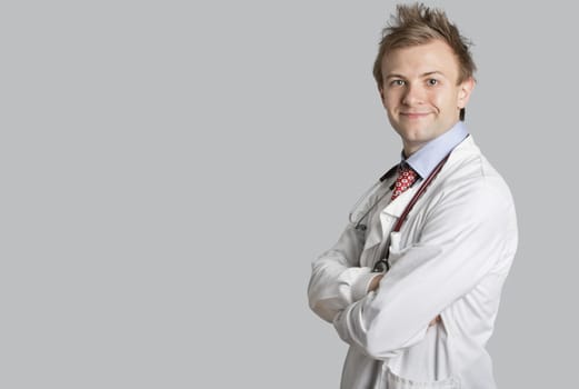 Portrait of a male doctor smiling with arms crossed over gray background