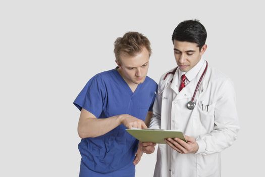 Doctor and male nurse discussing medical report over gray background