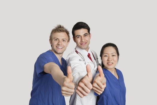 Portrait of a happy medical team gesturing thumbs up over gray background