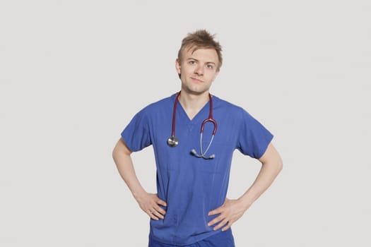 Portrait of male surgeon standing with hands on hips over gray background