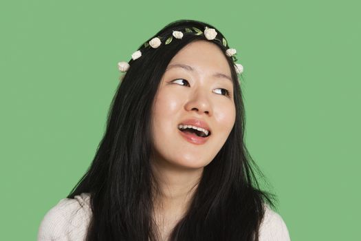 Young woman wearing hair ornament looking away over green background