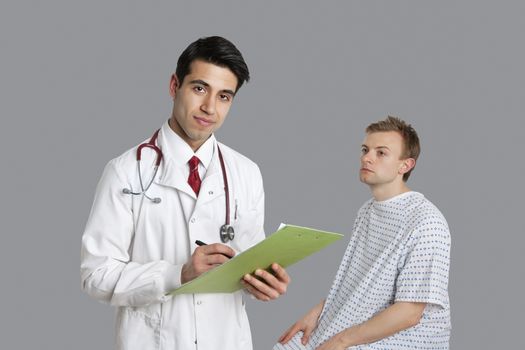 Portrait of Indian doctor writing on clipboard with patient sitting besides