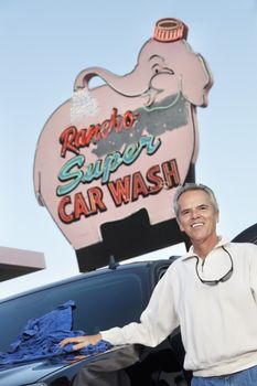 Portrait of mature owner of car wash standing below signboard with vehicle