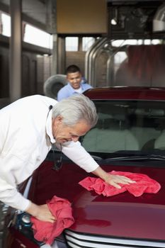 mature owner and young employee wiping vehicle with cloth in car wash