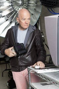 Senior photographer with camera using computer in studio
