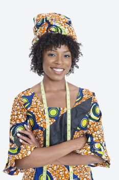 Portrait of young female fashion designer in African print attire standing hands folded over gray background