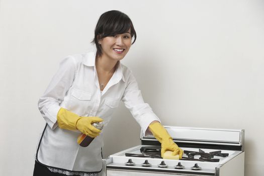 Portrait of young housemaid cleaning stove against gray background