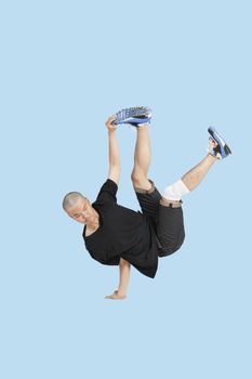 Break dancer performing handstand over blue background