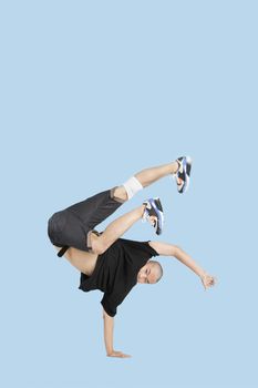 Male break dancer performing handstand over blue background