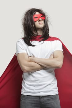 Young man in super hero costume standing with arms crossed against gray background