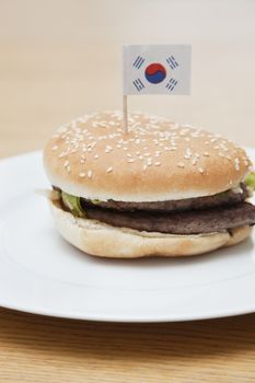 Fresh hamburger in plate with South Korean flag on wooden surface