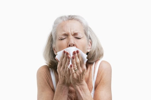 Senior woman sneezing into a tissue against white background