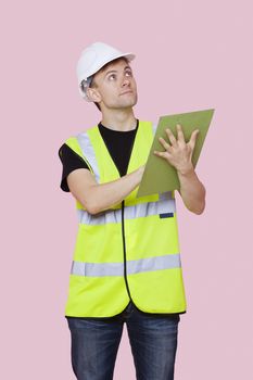 Male construction worker with clipboard looking away over pink background