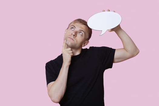 Thoughtful young man holding speech bubble while looking up over pink background