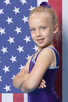 Portrait of a happy young female gymnast with arms crossed standing in front of American flag