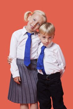 Portrait of young siblings in school uniform with arm around over orange background