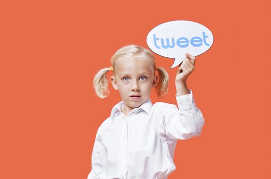 Portrait of a young girl holding tweet bubble against orange background