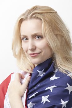 Portrait of beautiful young Caucasian woman wrapped in American flag against white background