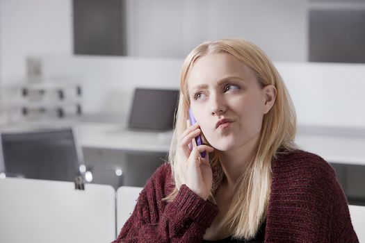 Thoughtful young businesswoman using cell phone at office