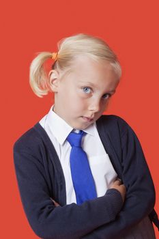 Portrait of a young schoolgirl with arms crossed over orange background