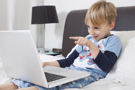 Playful Caucasian boy using laptop computer in bed