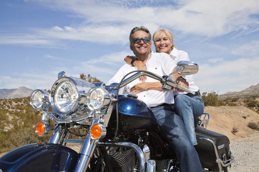 Senior couple on desert road sitting on motorcycle looking at camera