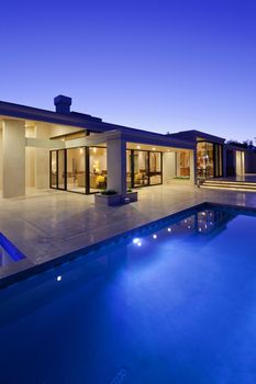 Rear view of luxury villa at night time with swimming pool