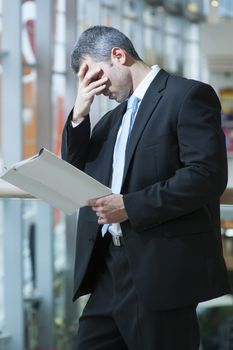 Business man reads document and covers face