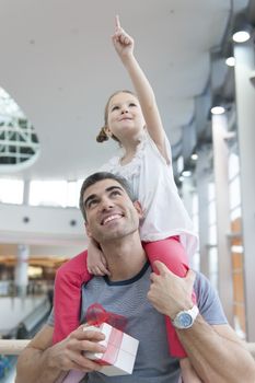 Young daughter points and sits on fathers shoulders