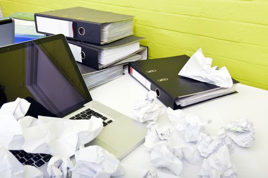 Close-up view of crumpled paper over laptop on desk with empty chair and folders