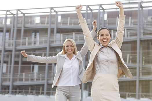 Excited young businesswomen with arms raised against office building