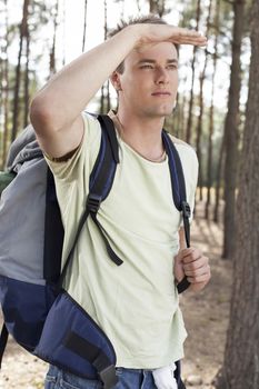 Young man with backpack shielding eyes in forest
