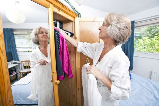 Senior woman selecting dress from closet at home