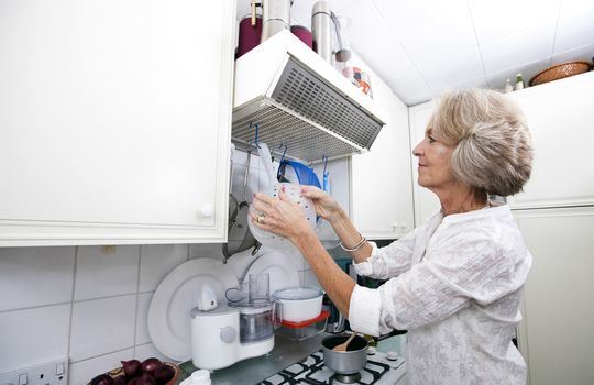 Senior woman hanging colander in domestic kitchen