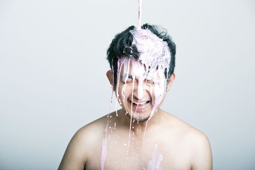 Shirtless young man with pink paint falling on his head against gray background