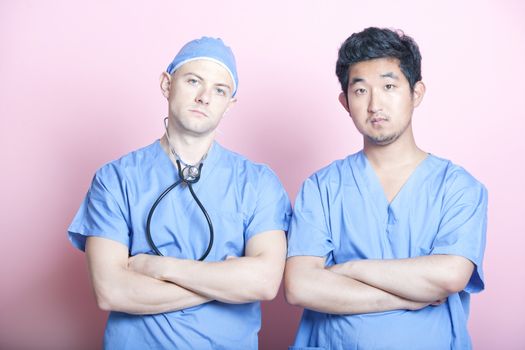 Portrait of two male surgeons standing with arms crossed over pink background