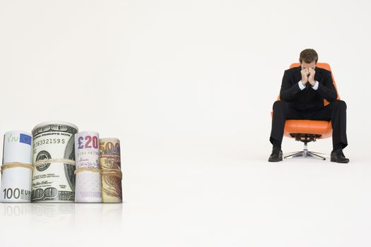 Money rolls with worried businessman on chair representing financial problems