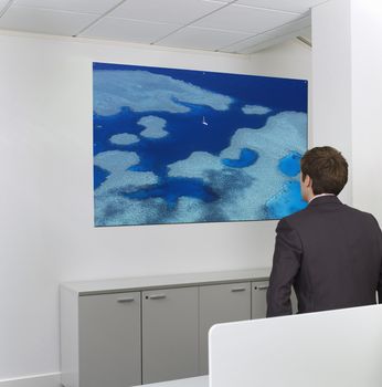 Contemplative mid-adult businessman looking at painting on wall in office