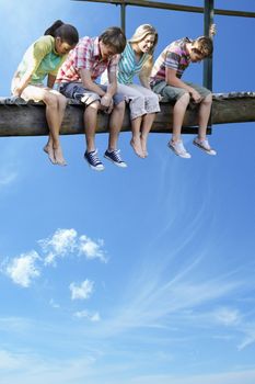 Four teenagers sitting on wooden bridge against blue sky