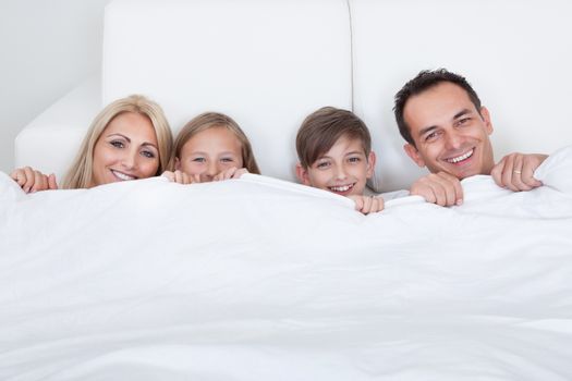 Happy Family With Two Children In Bed Under Cover