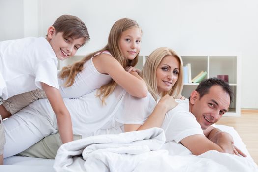 Happy Family With Two Children Lying Heaped On Bed