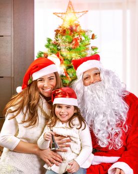 Happy cheerful young family celebrate Christmas holiday at home, little girl with mother and father wearing Santa Claus costume